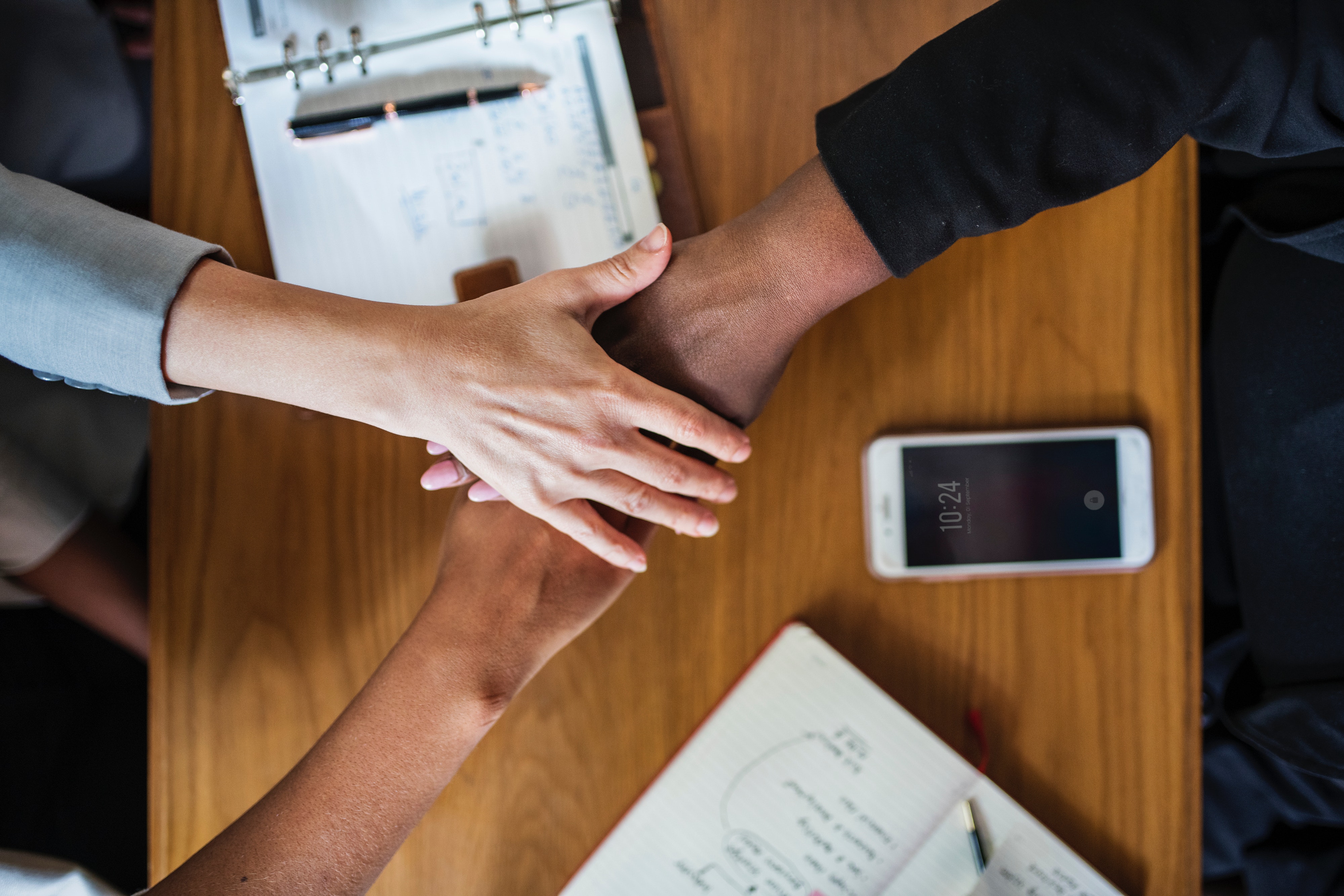 Three people crossing hands above diary and smartphone